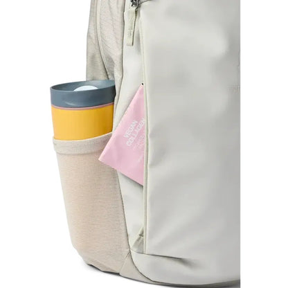 Side pocket of the Cotopaxi Allpa 18L Daypack in Mineral showing a yellow and gray tumbler and a pink item against a white background.