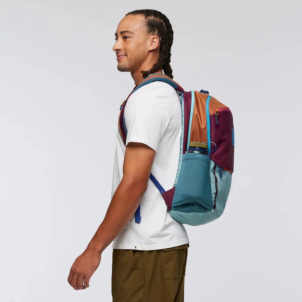 Side view of the Cotopaxi Allpa 26L Daypack - Del Dia showing the front pocket and model wearing it against a white background.