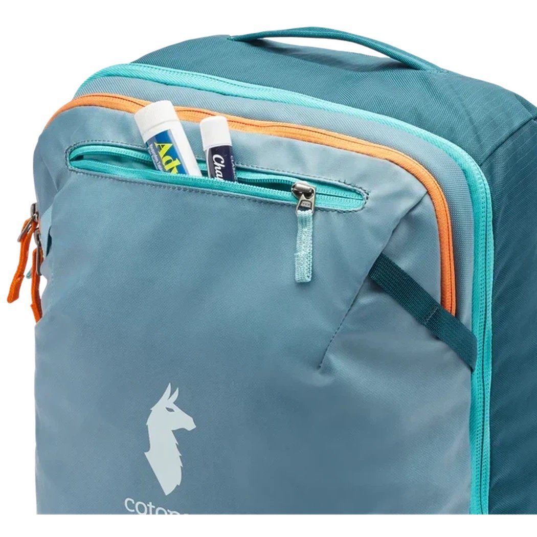 A front view of the Cotopaxi Allpa 28L Travel Pack in Blue Spruce/Abyss showing the front zippered pocket with two toiletries inside.