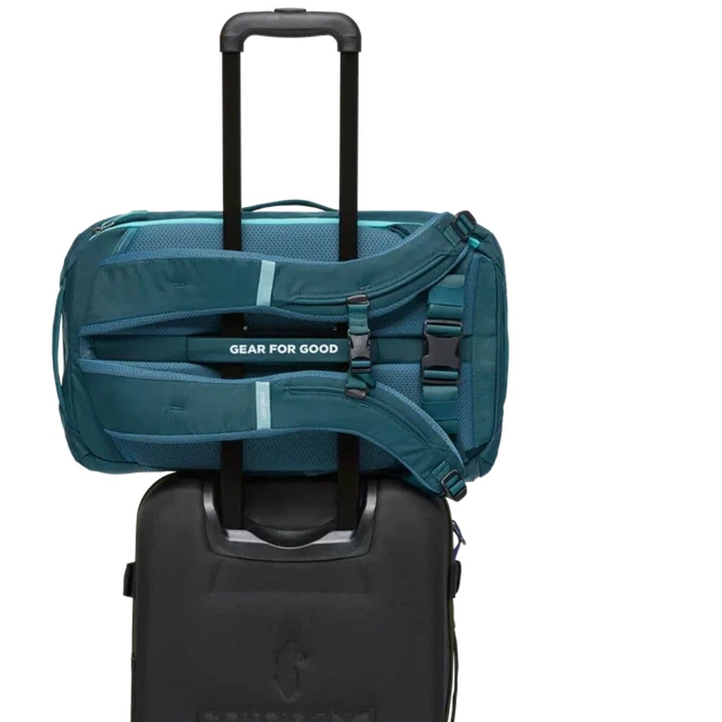 Back view of the Cotopaxi Allpa 28L Travel Pack in Blue Spruce/Abyss on top of a black rolling suitcase.