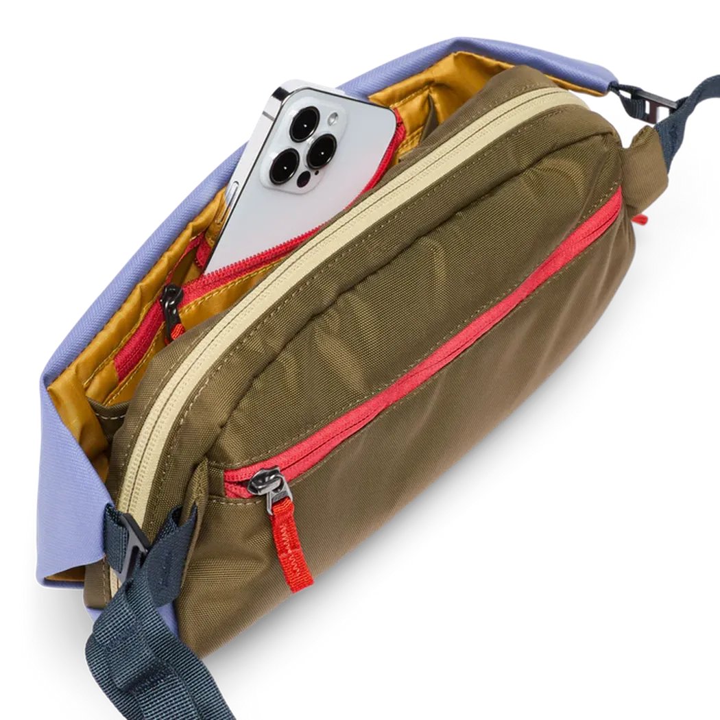 A side view of the Cotopaxi Coso 2L Hip Pack in Abyss/Coastal showing the red zipper and a smartphone inside against a white background.
