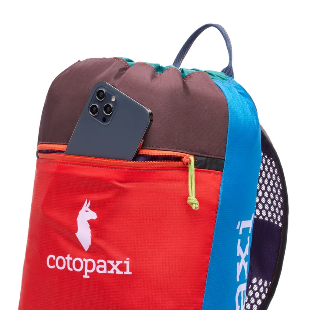 A red and blue Cotopaxi Del Dia daypack with a phone in the front pocket against a white background.