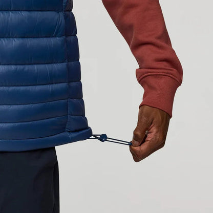 A model wearing the Cotopaxi Men's Fuego Down Vest in DeepSeaStripes adjusts the drawcord against a plain white background.