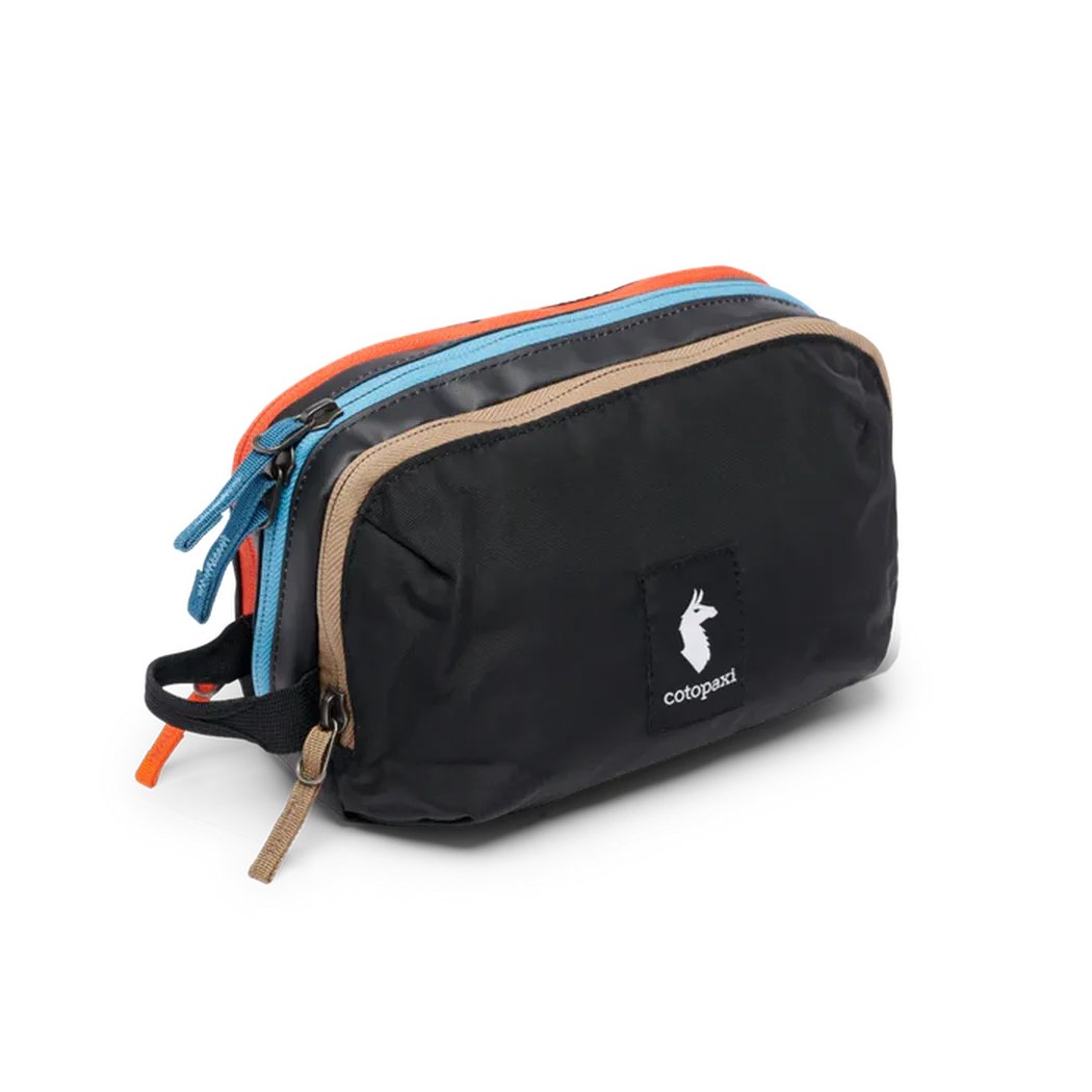 A front view of the Cotopaxi Nido Accessory Bag in Desert color showing the multiple zippers and logo patch against a white background.