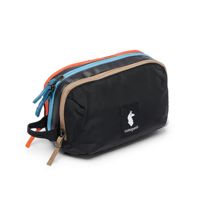 A front view of the Cotopaxi Nido Accessory Bag in Desert color showing the multiple zippers and logo patch against a white background.
