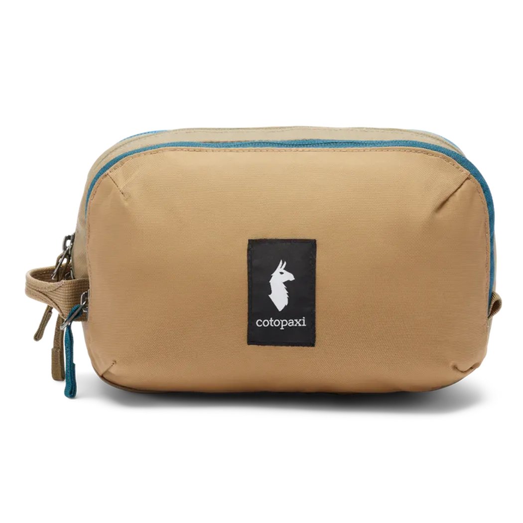 A front view of the Cotopaxi Nido Accessory Bag in Desert color with a black logo patch and blue zipper against a white background.