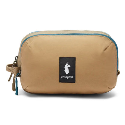 A front view of the Cotopaxi Nido Accessory Bag in Desert color with a black logo patch and blue zipper against a white background.