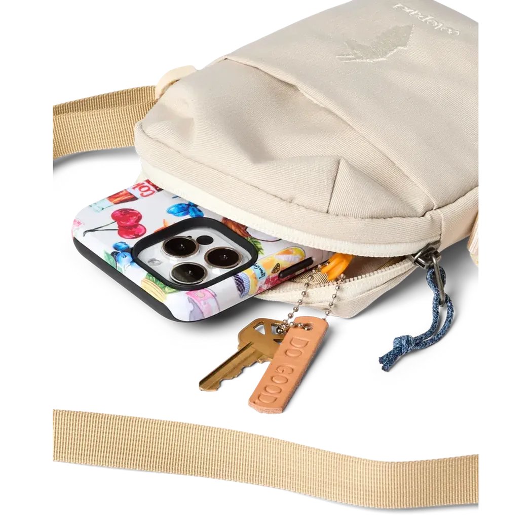 A close-up of the Cream Cotopaxi Todo 1L Shoulder Bag showing a colorful phone and keys spilling out of the open top pocket.