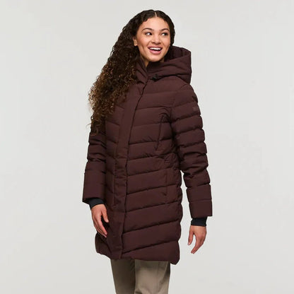 A woman wearing the Cotopaxi Women's Alivio Down Parka in Coffee stands against a plain white background.