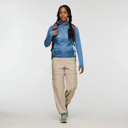 A woman wearing the Cotopaxi Women's Capa Hybrid Insulated Jacket in Fjord walks toward the camera against a plain white background.