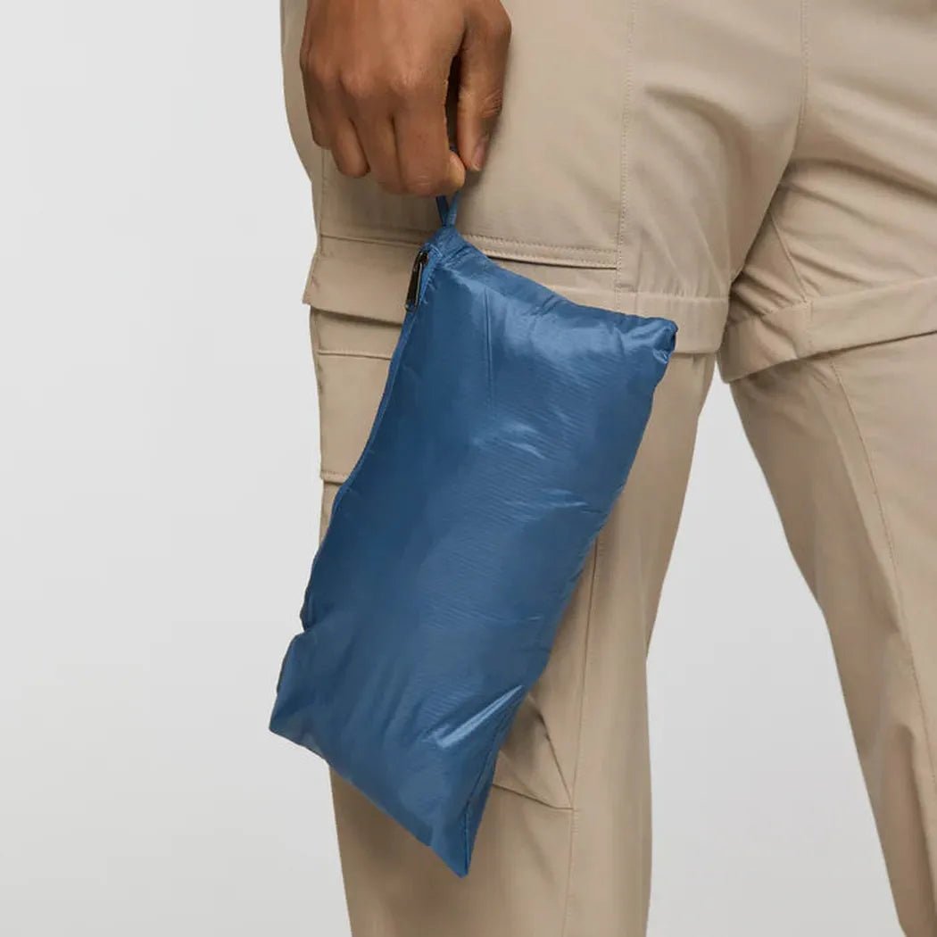 A model in beige cargo pants holds the blue Cotopaxi Women's Capa Hybrid Insulated Jacket against a plain white background.