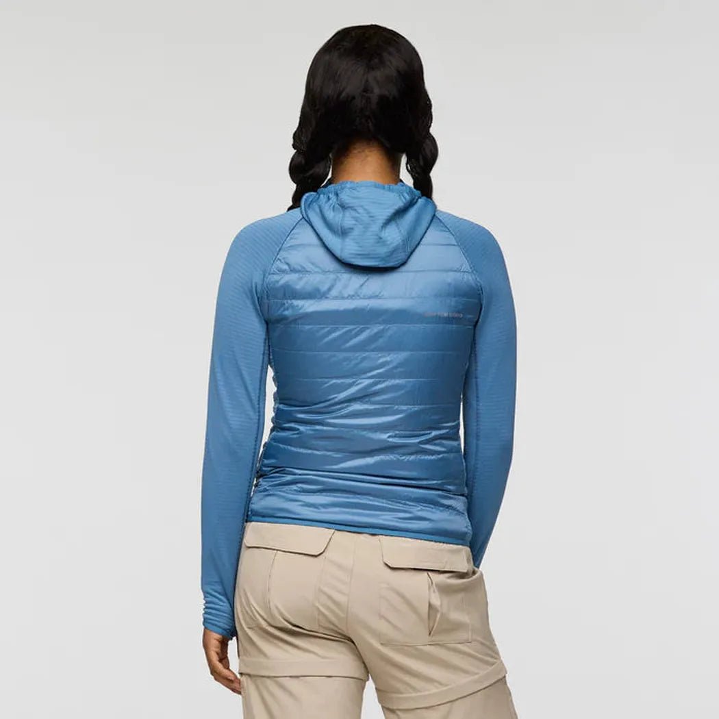Back view of the Cotopaxi Women's Capa Hybrid Insulated Jacket in Fjord, showing the hood and quilted back panel on a model wearing khaki pants against a plain background.