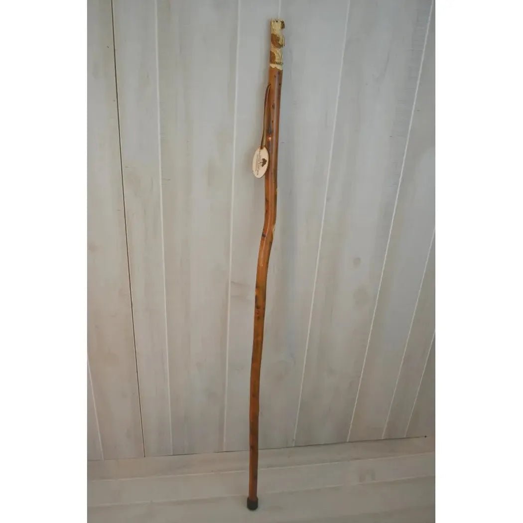 A full-length view of the Creation Carvings Walking Stick with Bear Carving against a light wood-paneled background.