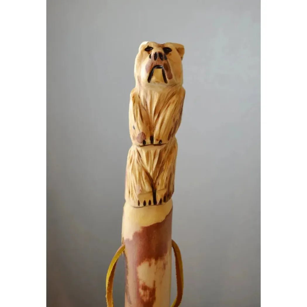 A top-down view of the Creation Carvings Walking Stick with Bear Carving, showing the detailed bear carving and the stick's natural wood color against a gray background.