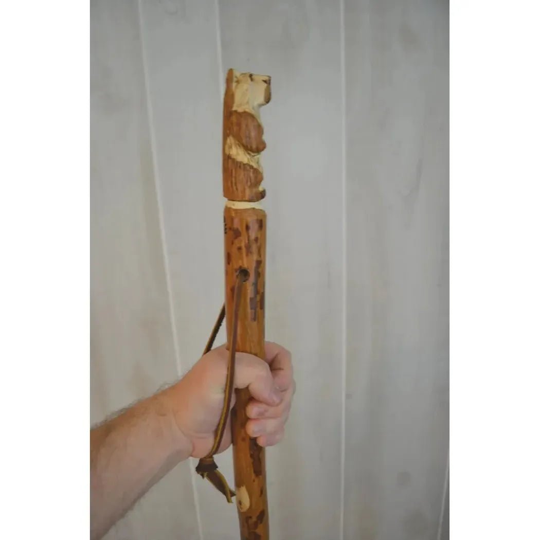 A hand holds a Creation Carvings Walking Stick with Bear Carving against a light gray background.