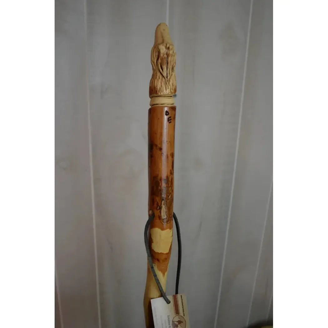 A close-up of the Creation Carvings Walking Stick with Wolf Head Craving, showing the detailed carving and natural wood texture against a light background.