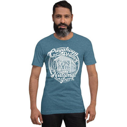A front view of the Cuyahoga Valley Clothing Company CVNP Covered Bridge T - Shirt in Heather Deep Teal worn by a man against a white background.