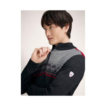 A man wearing the Dale Of Norway Liberg Masc Sweater-SAMPLE in DChrclSmkRedros poses with his hand near his face against a plain background.