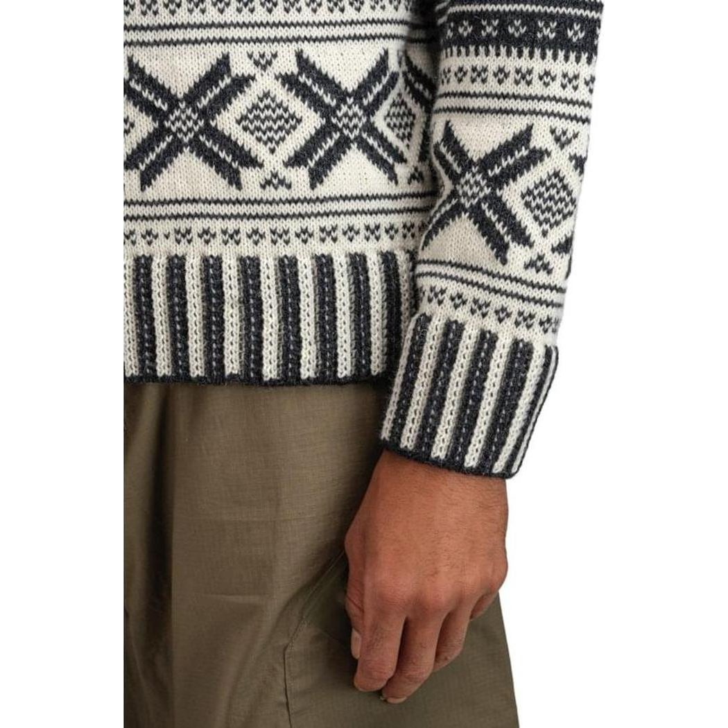 A close-up of the Dale Of Norway Men's Torridal Sweater in Darkcharcoal Offwhite, showing the patterned design and cuff on a model wearing brown pants.