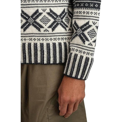 A close-up of the Dale Of Norway Men's Torridal Sweater in Darkcharcoal Offwhite, showing the patterned design and cuff on a model wearing brown pants.