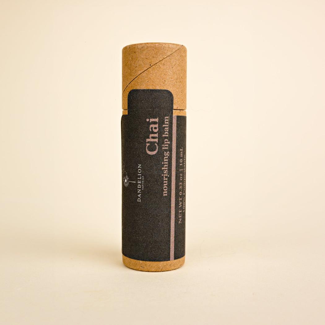 A side view of the Dandelion Naturals Chai Lip Balm in a brown tube with a black label against a plain background.
