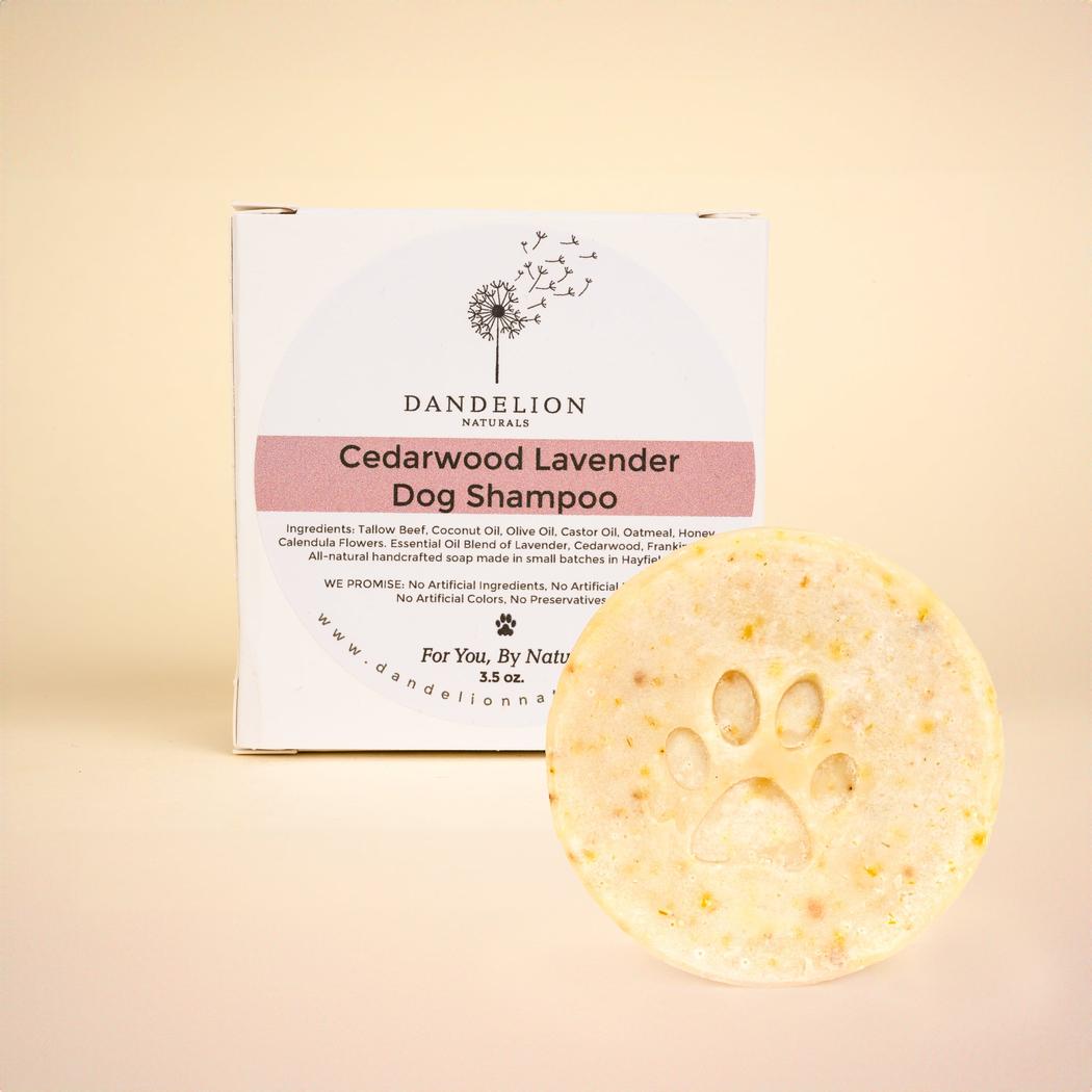 A front view of the Dandelion Naturals Cedarwood Lavender Dog Shampoo Bar with a paw print on it in front of its box against a light background.