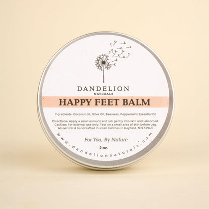 A round tin of Dandelion Naturals Happy Feet Balm sits centered against a plain beige background.