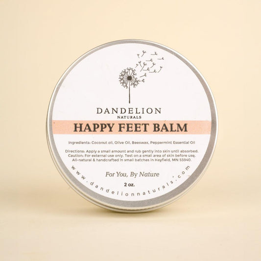 A round tin of Dandelion Naturals Happy Feet Balm sits centered against a plain beige background.