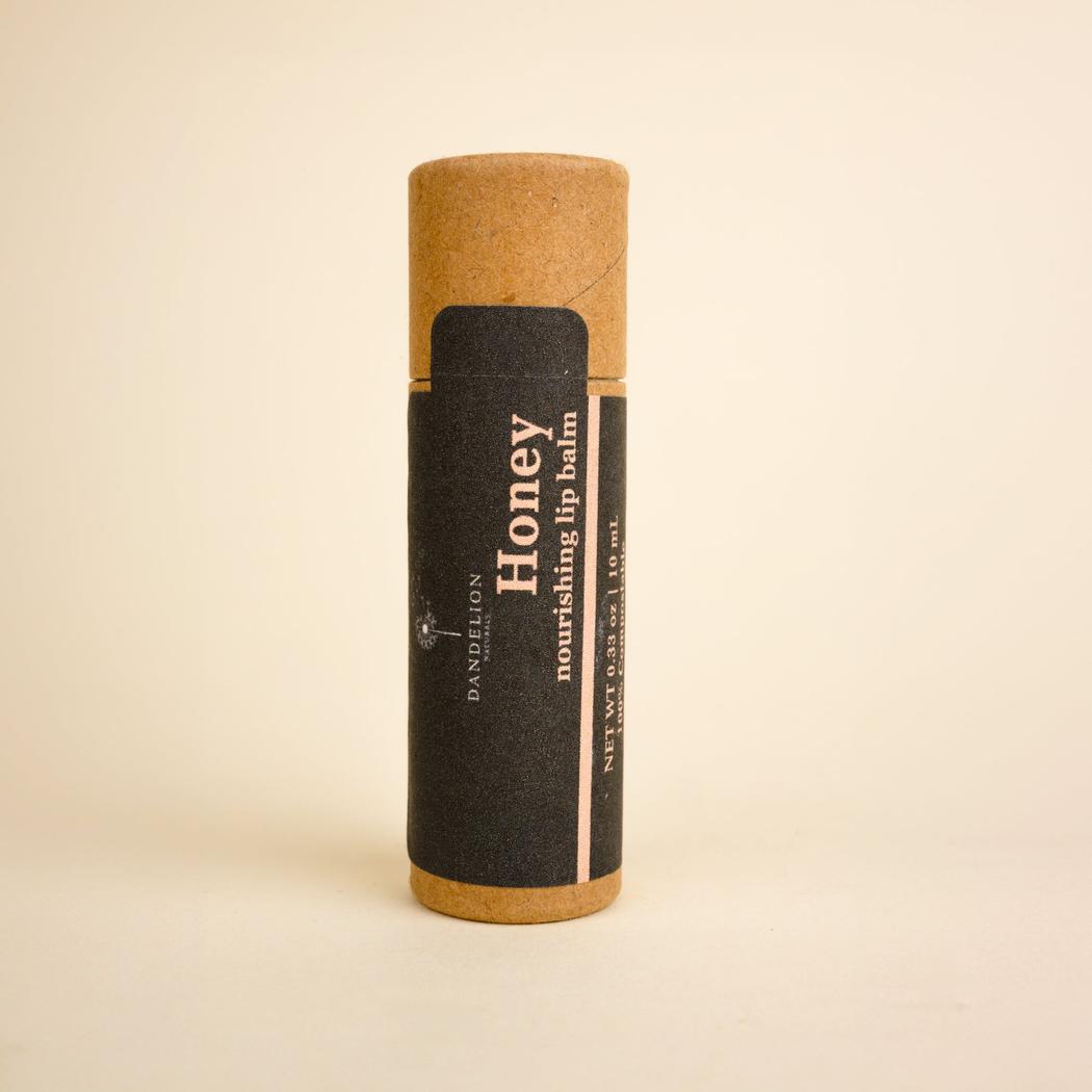 A front view of the Dandelion Naturals Honey Lip Tallow Balm with a black label and brown cap against a plain background.