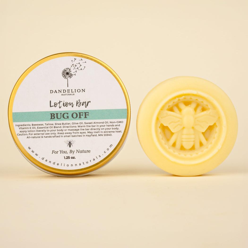 A round tin of Dandelion Naturals Lotion Tallow Bar - Natural Bug Repellant sits next to a yellow bar with a bee design, against a plain background.