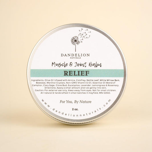 A round tin of Dandelion Naturals Relief Muscle and Joint Balm sits centered on a plain beige background.