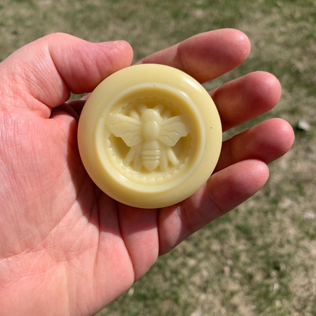 A hand holds the Dandelion Naturals Rose Lavender Vanilla Tallow Lotion Bar against a grassy outdoor background.