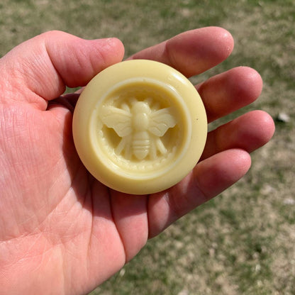 A hand holds the Dandelion Naturals Rose Lavender Vanilla Tallow Lotion Bar against a grassy outdoor background.