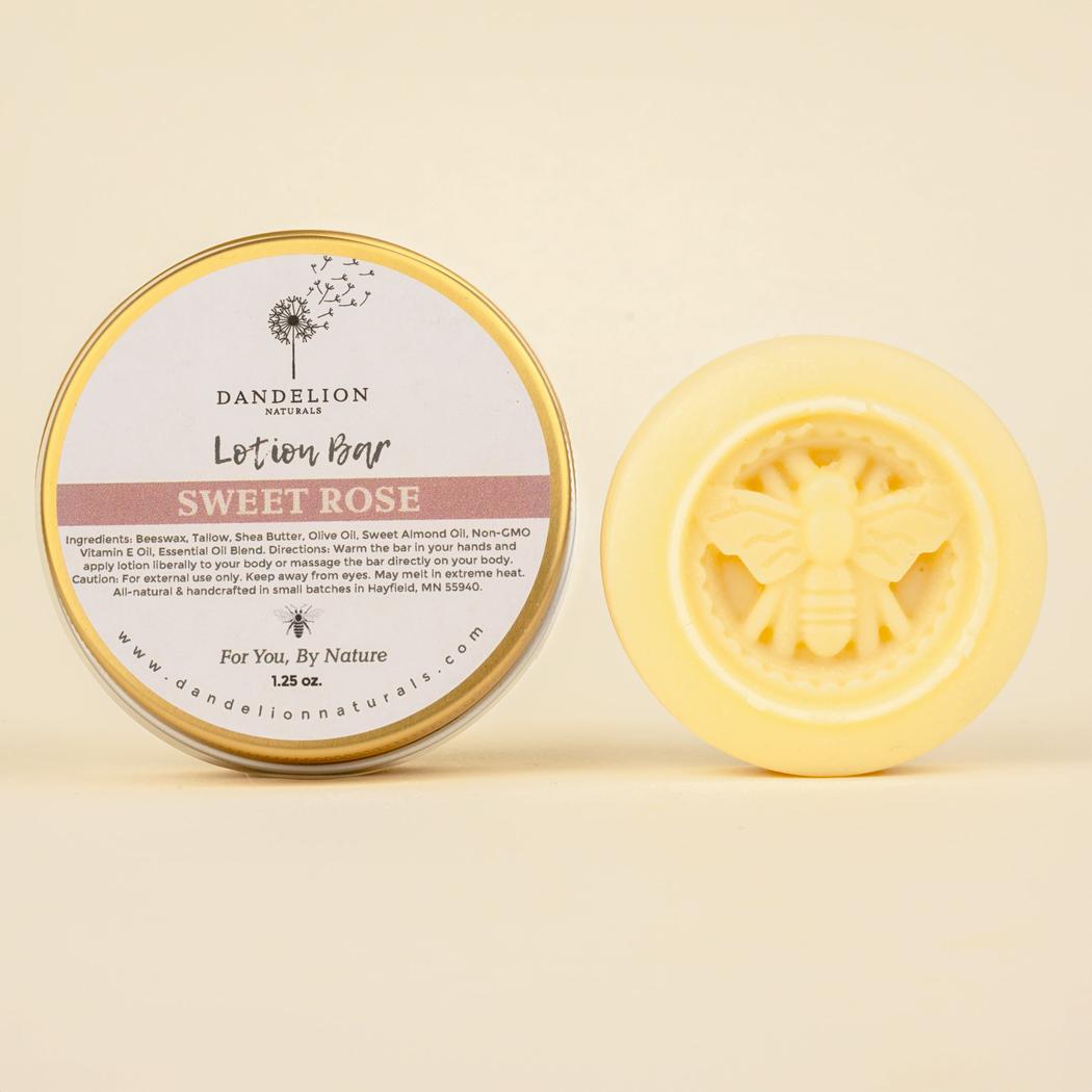 A round tin of Dandelion Naturals Rose Lavender Vanilla Tallow Lotion Bar sits next to a yellow bar with a bee design, both against a light background.