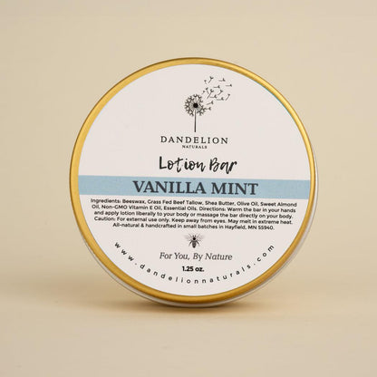 A front view of the Dandelion Naturals Vanilla Mint Tallow Lotion Bar in a round tin with a gold rim against a plain beige background.