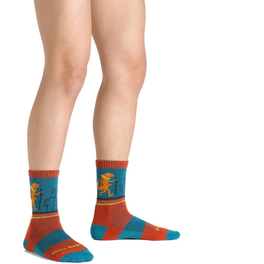 Side view of the Darn Tough Kid's Sal Micro Crew Lightweight With Cushion socks in Lava, showing the colorful dinosaur design on a model's legs against a white background.