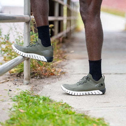 A man wearing Darn Tough Men's Solid Crew Lightweight Black socks stands on a sidewalk near a railing.