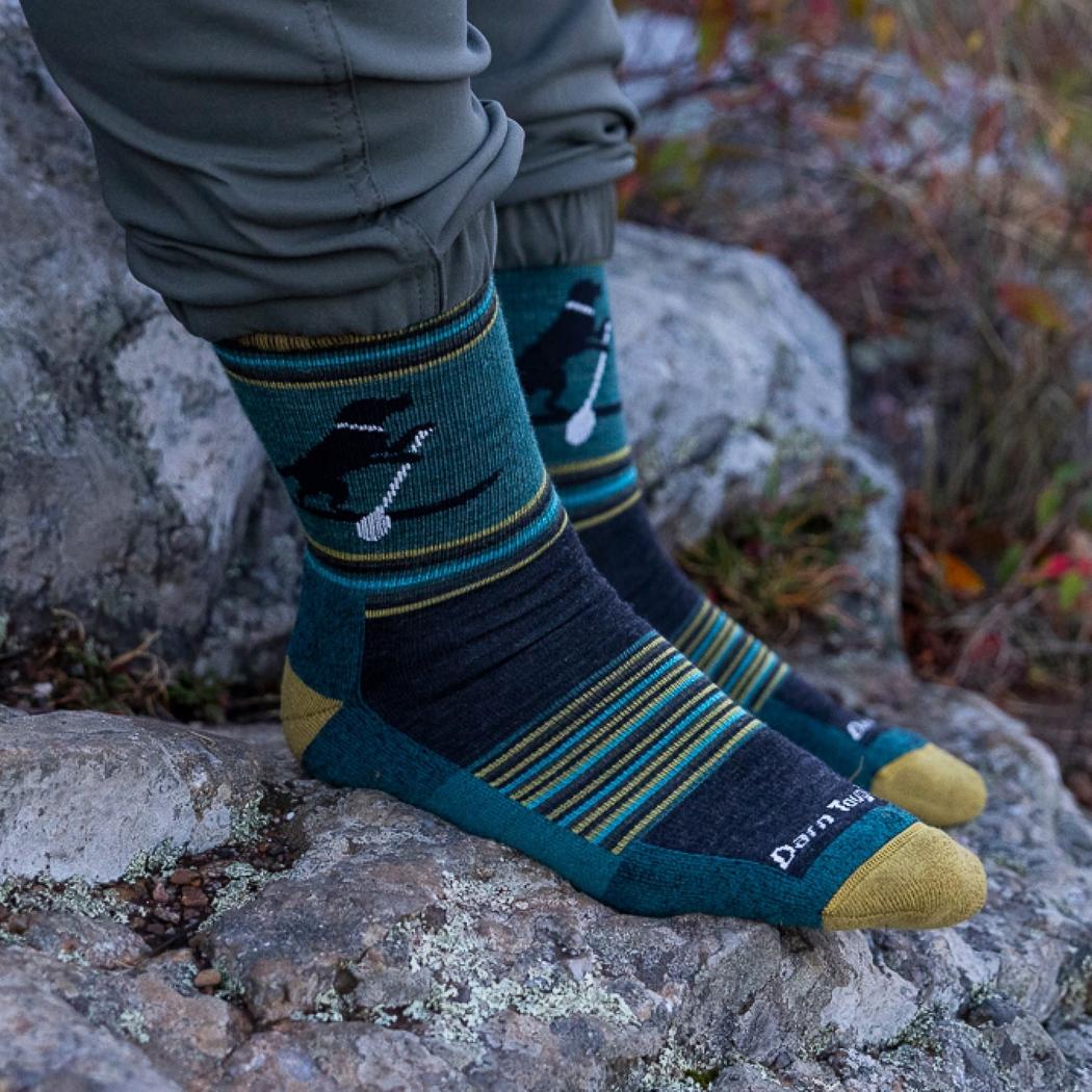 A person wearing Dog Pond Darn Tough Men's Willoughby Micro Crew Lightweight Hiking Socks sits on a rock with a forest background.