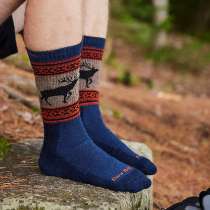 A person wearing Charcoal Darn Tough Vangrizzle Boot Midweight with Cushion socks stands on a rock in a forest.