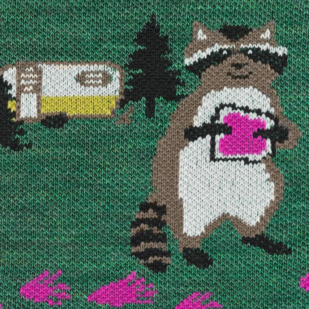 A close-up of the Darn Tough Women's Critter Club Micro Crew Lightweight with Cushion in Bark, showing a raccoon holding a pink object and a camper on a green background.