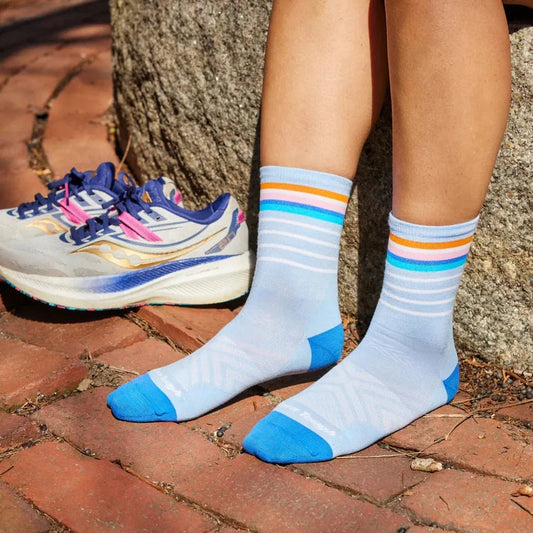 A woman’s legs in Sky Darn Tough Women's Stride Micro Crew Ultra-Lightweight socks stand on brick next to a running shoe.