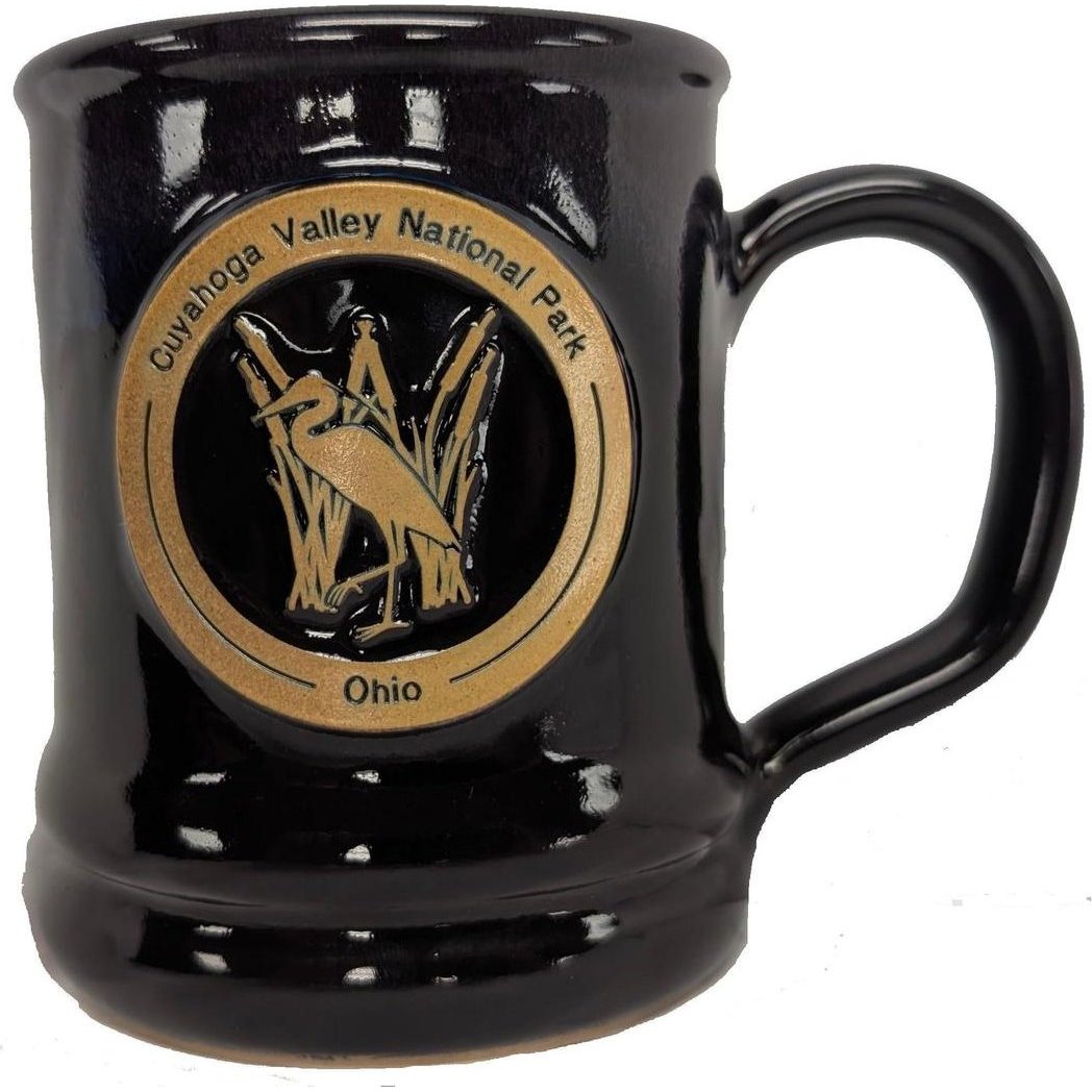 A black Deneen Pottery Cuyahoga Valley National Park Mug with a gold emblem, shown from the front against a white background.