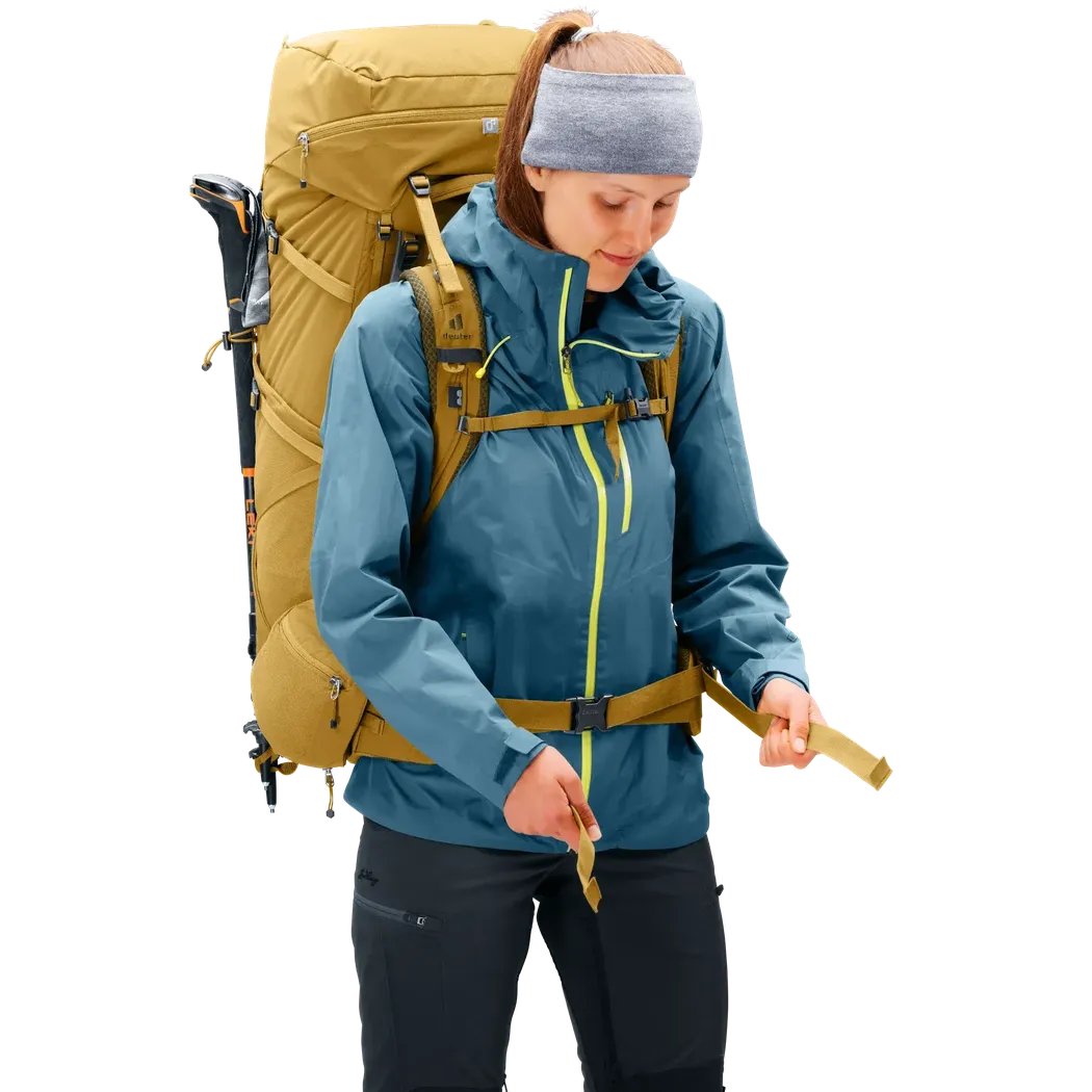 A woman wearing the Deuter Aircontact Core 55+10 SL backpack in Savanna Nori adjusts straps against a white background.