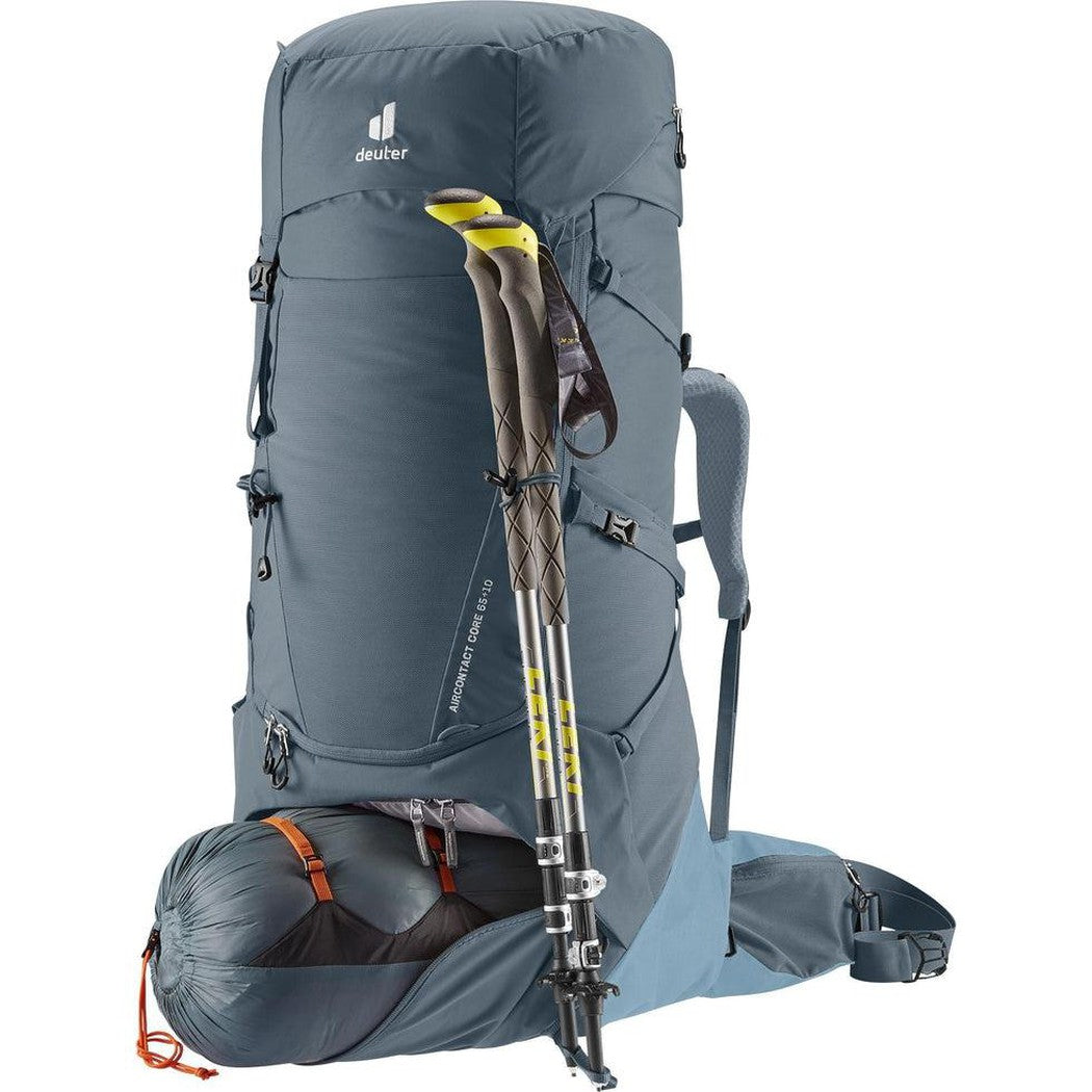 A front view of the Deuter Aircontact Core 65 + 10 backpack in Graphite Shale with trekking poles and a rolled sleeping bag attached, set against a white background.