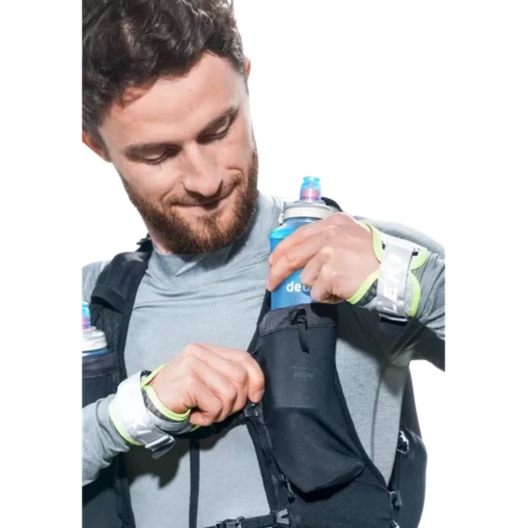 A man puts a blue Deuter flask into the pocket of a black Deuter Ascender 13 backpack against a white background.