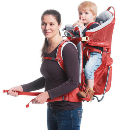 A woman wears the Deuter Kid Comfort Active SL in Currant with a child in the carrier, shown from the front against a white background.