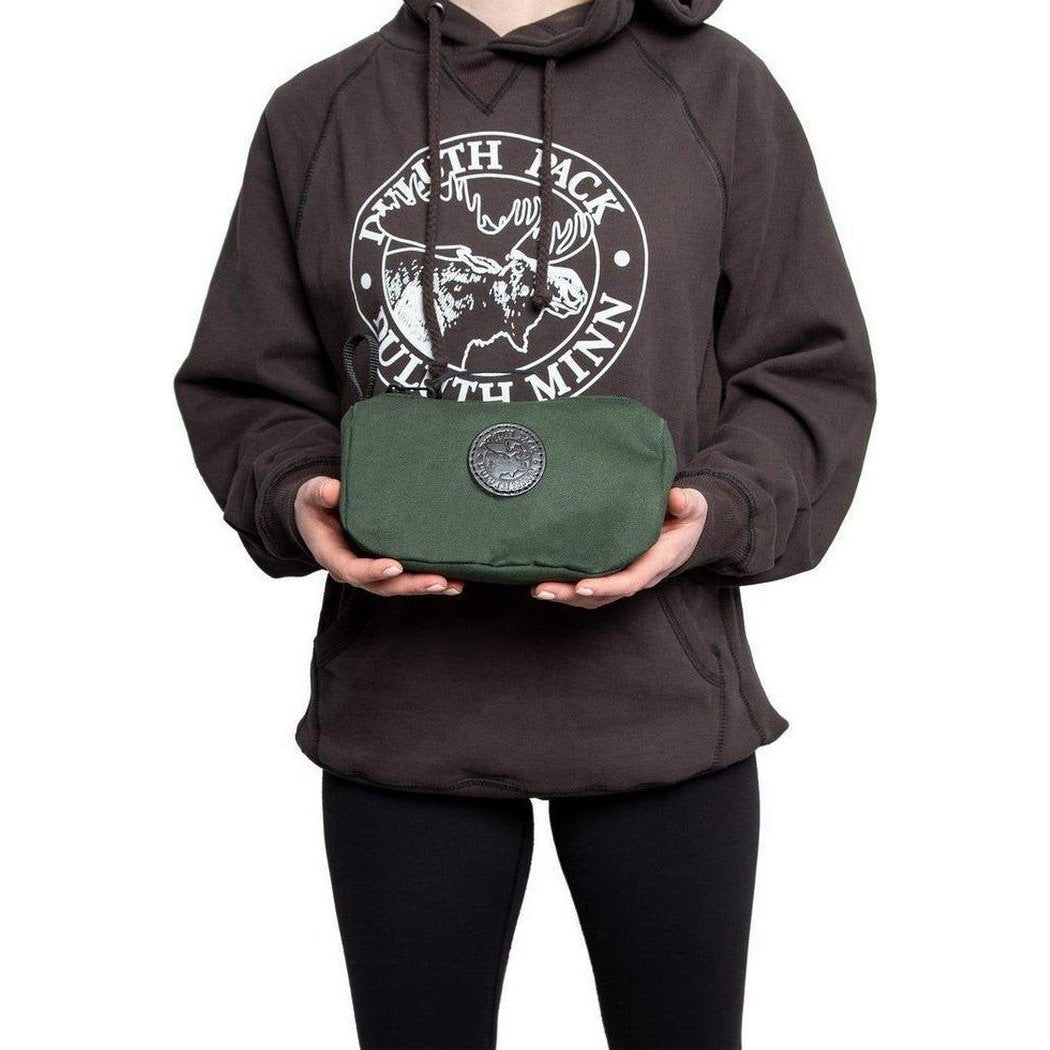 A model wearing a charcoal hoodie holds the green Duluth Pack Grab-N-Go Bag with a circular logo against a white background.