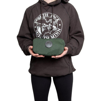 A model wearing a charcoal hoodie holds the green Duluth Pack Grab-N-Go Bag with a circular logo against a white background.