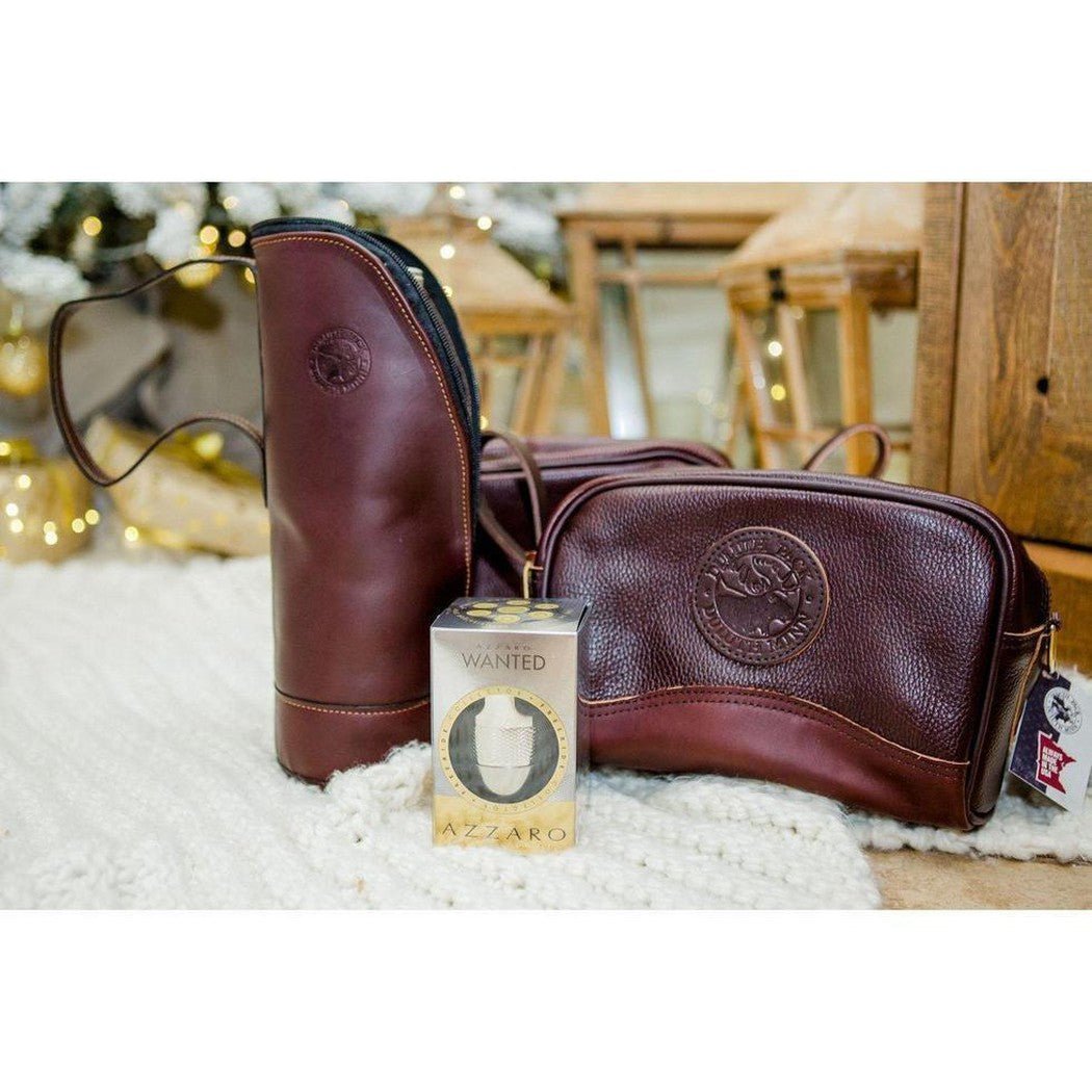 A brown smooth Duluth Pack Leather Sportsman's Kit Bag sits on a white rug with a wanted azzaro box in front and a wooden background.
