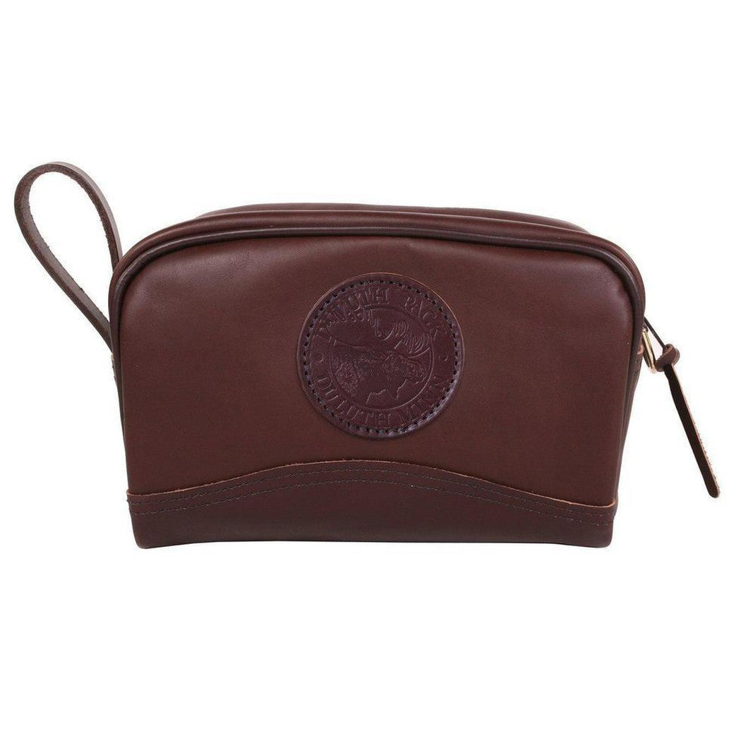 A brown smooth Duluth Pack Leather Sportsman's Kit Bag with a circular logo and zipper pull, shown from the front against a white background.